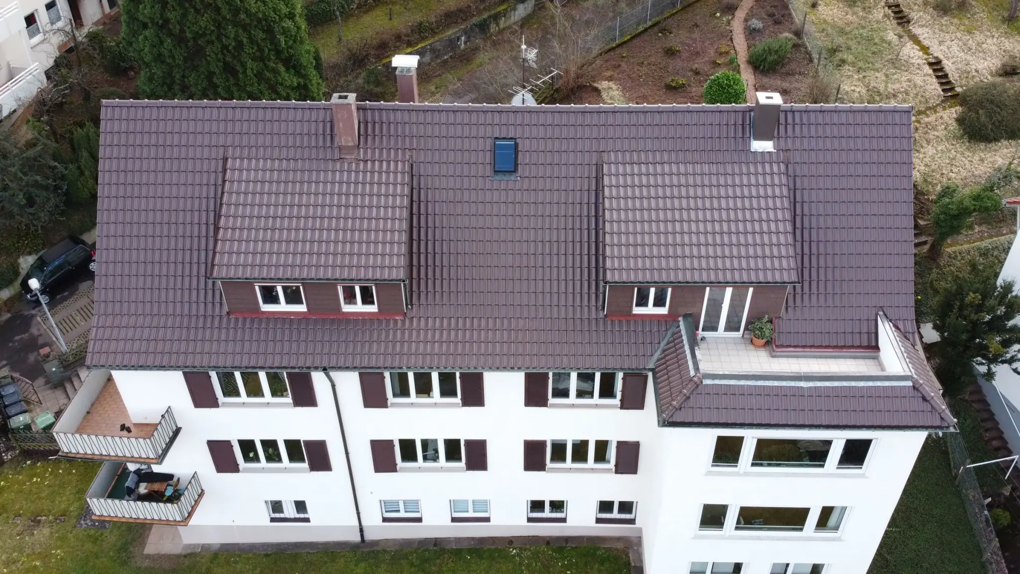 Dasselbe Mehrfamilienhaus nach der Sanierung: neu eingedecktes Ziegeldach, Gauben und Dachterrasse